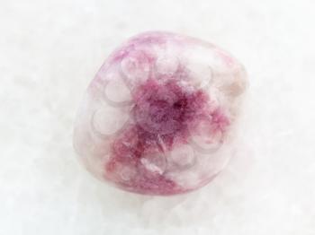 macro shooting of natural mineral rock specimen - tumbled pink Sodalite gemstone on white marble background from Russia