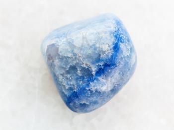 macro shooting of natural mineral rock specimen - tumbled blue dyed agate gemstone on white marble background