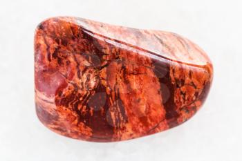 macro shooting of natural mineral rock specimen - tumbled Brecciated red jasper gemstone on white marble background