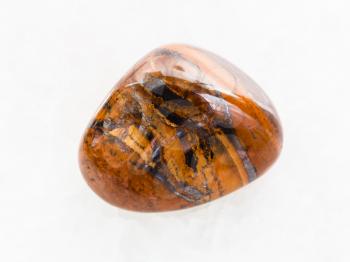 macro shooting of natural mineral rock specimen - polished tigers eye gemstone on white marble background