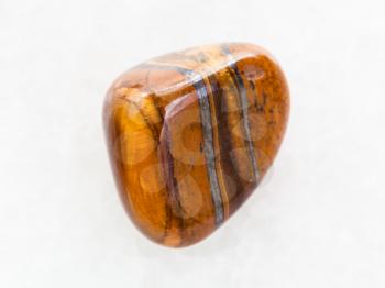 macro shooting of natural mineral rock specimen - tumbled tigers eye gemstone on white marble background