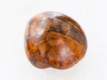 macro shooting of natural mineral rock specimen - polished tiger-eye stone on white marble background