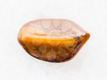 macro shooting of natural mineral rock specimen - tumbled tiger's eye gemstone on white marble background from South Africa