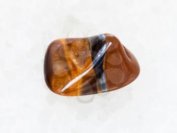 macro shooting of natural mineral rock specimen - tumbled tiger eye gemstone on white marble background from South Africa