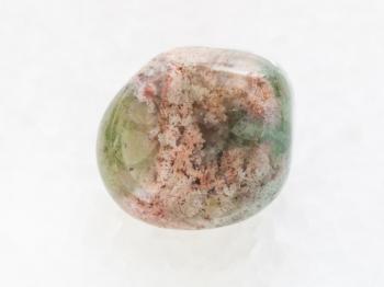 macro shooting of natural mineral rock specimen - tumbled Moss Agate gemstone on white marble background