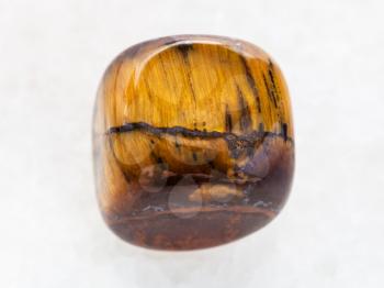 macro shooting of natural mineral rock specimen - tumbled tiger-eye gem stone on white marble background