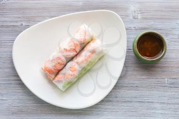 top view of served Nem cuon (fresh Vietnamese nem roll with shrimps, mango and ginger) on white plate on wooden table