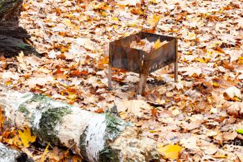 abandoned small barbecue grill with trash on meadow covered by fallen leaves in city park in autumn