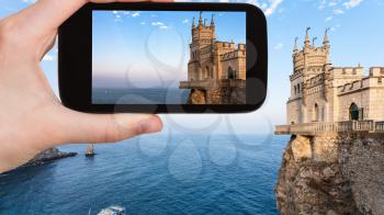 travel concept - tourist photographs Swallow's Nest castle over Black Sea on Crimean Southern Coast in Crimea in september evening on smartphone