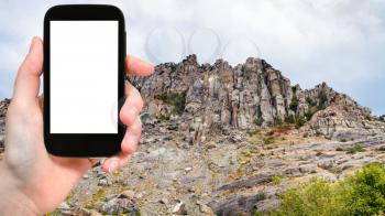travel concept - tourist photographs old rocks at Demerdzhi (Demirci) Mountain from The Valley of Ghosts in Crimea in september on smartphone with cut out screen for advertising logo