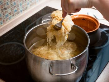 cooking soup - the cook moves stewed sauerkraut from ceramic pot into saucepan with meat broth