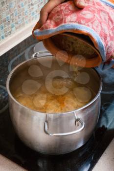 cooking soup - the cook puts stewed sauerkraut from ceramic pot into saucepan with meat broth