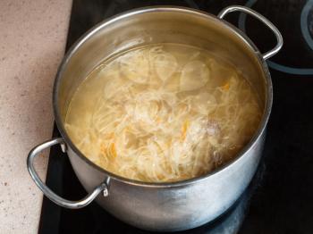 cooking soup - cabbage soup with stewed sauerkraut in stewpan on ceramic cooker