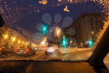 driving in night snowfall in Moscow - defocused background with view from melting snow on car windshield in evening