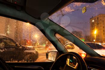 wet windscreen during driving in Moscow city in winter evening in snow (focus on car windscreen glass)