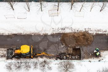 above view of workers and tractor digging road to change sewer pipes in winter in Moscow city