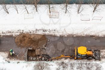 top view of workers and excavator digging road to change sewer pipes in winter in Moscow city