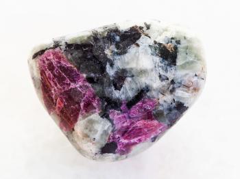 macro shooting of natural mineral stone specimen - tumbled pink Corundum crystals in rock on white marble background