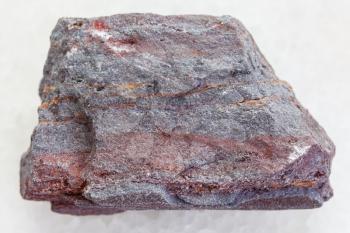 macro shooting of natural mineral rock specimen - piece of jaspilite (ferruginous quartzite) stone on white marble background