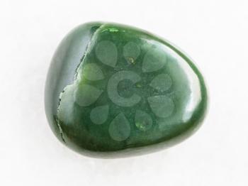 macro shooting of natural mineral rock specimen - tumbled green nephrite gemstone on white marble background