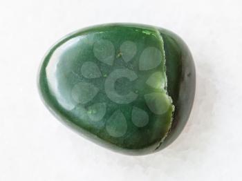 macro shooting of natural mineral rock specimen - pebble of green nephrite gemstone on white marble background