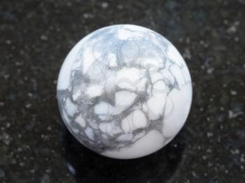 macro shooting of natural mineral rock specimen - ball from Howlite gemstone on dark granite background