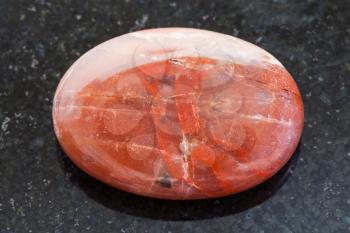 macro shooting of natural mineral rock specimen - bead from red Mookaite (Mookaite Jasper) gemstone on dark granite background
