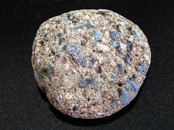 macro shooting of natural mineral rock specimen - pebble of Arkose sandstone on dark granite background