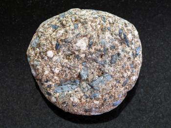 macro shooting of natural mineral rock specimen - tumbled Arkose sandstone on dark granite background