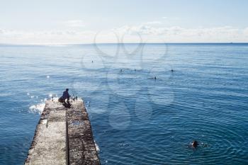 travel to Crimea - fisherman on pier and swimming people in Black Sea in Alushta city in morning