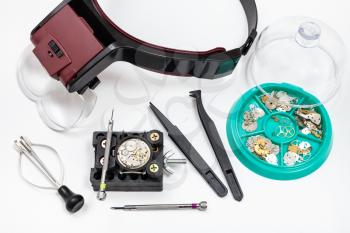 watchmaker workshop - above view of kit of tools with head-mounted magnifier and spare parts for repairing mechanical watch on white background