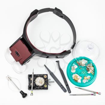 watchmaker workshop - top view of set of tools with head-mounted magnifier and spare parts for repairing mechanical watch on white background