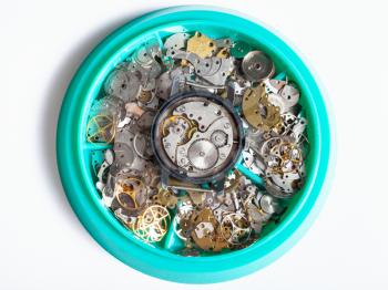 watchmaker workshop - top view of disassembled watch in plate with clock spare parts on white background