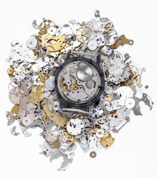 watchmaker workshop - top view of open mechanical watch on heap of old clock spare parts on white background