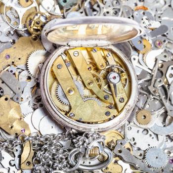 watchmaker workshop - open retro silver pocket watch with brass clockwork on heap of clock spare parts