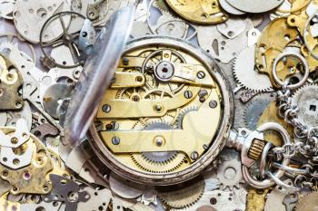 watchmaker workshop - open vintage silver pocket watch with brass clockwork on heap of clock spare parts