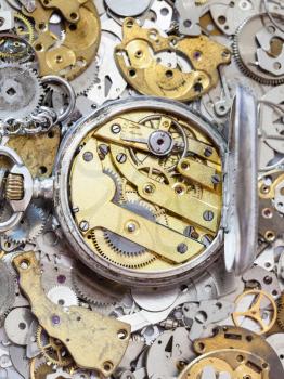 watchmaker workshop - open old silver pocket watch with brass clockwork on pile of clock spare parts