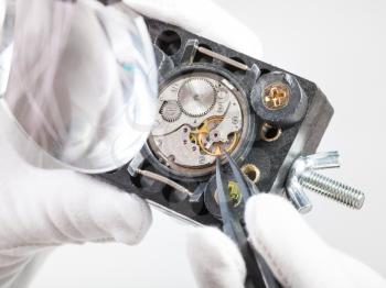 watchmaker workshop - watchmaker in head-mounted magnifier repairs old mechanical wristwatch with tweezers