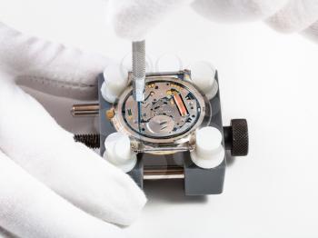 watchmaker workshop - repairing quartz wristwatch close up with screwdriver on white background