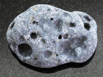 macro shooting of natural mineral rock specimen - tumbled gray pumice stone on dark granite background from Sicily