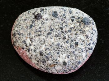 macro shooting of natural mineral rock specimen - pebble of gray Arkose sandstone on dark granite background