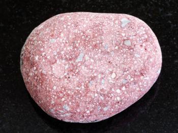 macro shooting of natural mineral rock specimen - pebble of pink Arkose sandstone on dark granite background