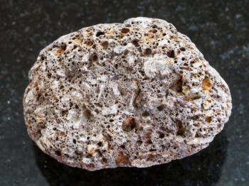 macro shooting of natural mineral rock specimen - pebble of brown pumice stone on dark granite background from Sicily