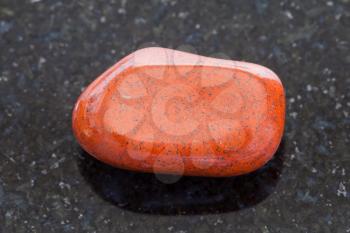macro shooting of natural mineral rock specimen - tumbled red jasper gemstone on dark granite background