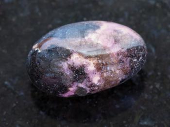 macro shooting of natural mineral rock specimen - polished Rhodonite gemstone on dark granite background