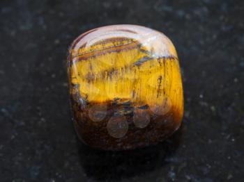 macro shooting of natural mineral rock specimen - tumbled tiger-eye gem stone on dark granite background