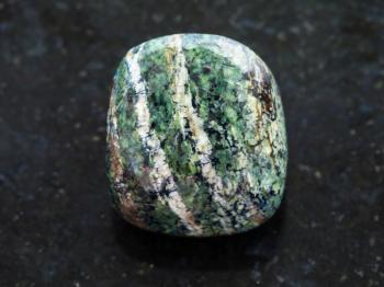 macro shooting of natural mineral rock specimen - polished chrysotile gemstone on dark granite background