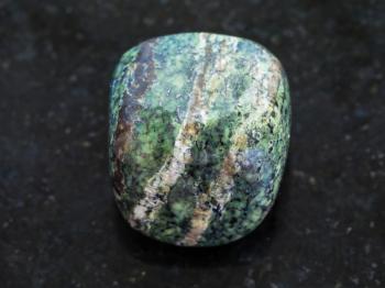 macro shooting of natural mineral rock specimen - tumbled chrysotile gemstone on dark granite background