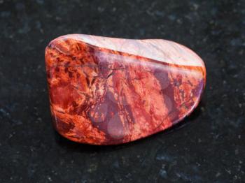 macro shooting of natural mineral rock specimen - tumbled Brecciated red jasper gemstone on dark granite background