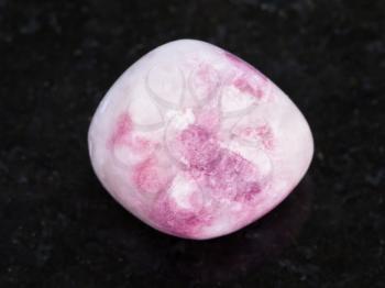 macro shooting of natural mineral rock specimen - tumbled pink Sodalite gemstone on dark granite background from Russia